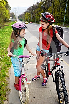 Girls children cycling on yellow bike lane. There are cars on road.