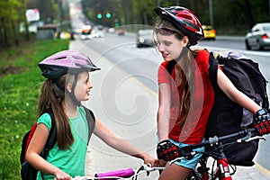 Girls children cycling on yellow bike lane. There are cars on road.