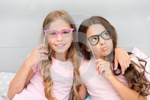 Girls children posing with grimaces photo booth props. Pajamas party concept. Girls friends having fun pajamas party