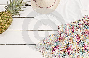 Girls clothes and accessories collage. Straw hat, floral dress, pineapple. White Old Wooden Background