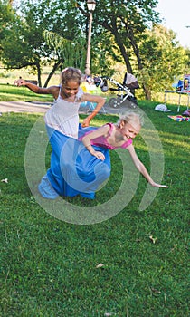 Girls compete in a relay race . Jumping in bags . They laugh and fall .