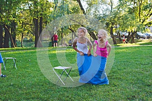 Girls compete in a relay race . Jumping in bags . They laugh and fall .