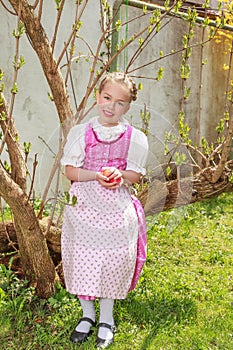 Girls in the dirndl sit in the garden and plays laughing with Easter eggs
