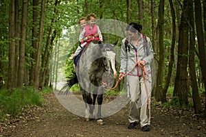 Girls enjoying horseback riding in the woods with mother, young pretty girls with blond curly hair on a horse, freedom