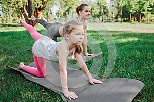 Girls are excercising outside in park. They are stretching their left legs and leaning on both hands and right legs