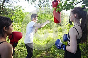 Girls fighting boxing outside with coach in green park, sport summer people concept