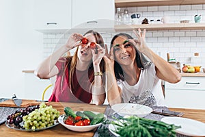 Girls fooling around in the kitchen playing with vegetables.