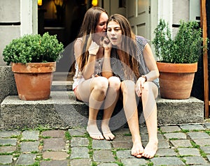 Girls friend sitting on the steps of the cafe and whispering.