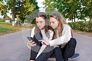 Girls girlfriends teenagers, summer in park, video on phone, rest after school. SMS on smartphone. Read write message