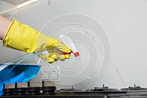 A girls hand with a cleaning spray sprays on a built-in gas stove. Modern anti-grease, antistatic cleaning product