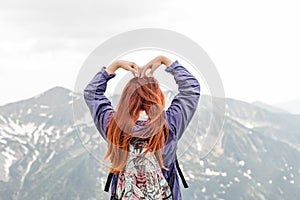 Girls hand to make a heart shape. Copyspace. A young pretty redheaded woman standing on a background of mountains. Trekking,