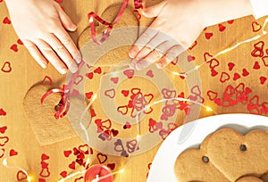 Girls hands making garland from the homemade baked heart cookies on the background.