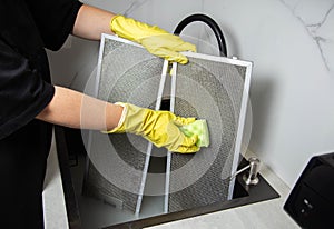 A girls hands in yellow gloves with a sponge wash the kitchen hood filter with detergent to remove grease and dirt