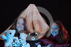 Girls with happy faces playing with teddies under blanket