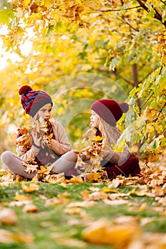 Girls in the hat sit in autumn Park with maple leaf  and play, have fun