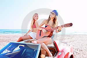 Girls having fun playing guitar on th beach in a car