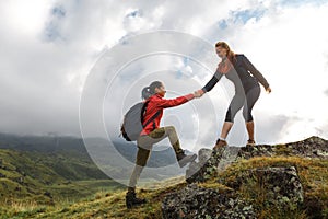 Girls helping each other hike up a mountain at sunrise. Giving a