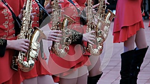 Girls in hussar red clothes and black boots play saxophones. Close-up. The brass band Kostanay.