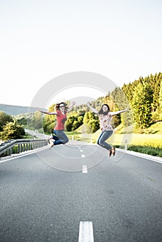 Girls jumping in the middle of road. Friendship