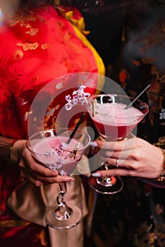 Girls in kimano are holding two red cocktails decorated with pink flowers