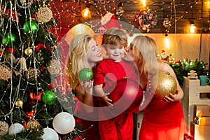 Girls are kissing their lovely little brother by the Christmas tree. Christmas decoration. Happy new Year.