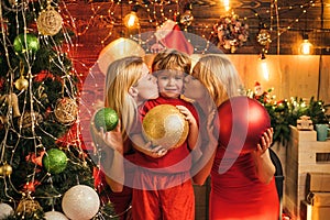 Girls are kissing their lovely little brother by the Christmas tree. Ready to the party. Christmas decoration.