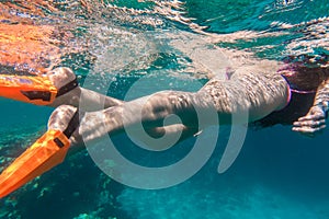Girls legs in orange flippers dive underwater in sea near coral