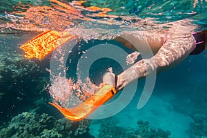 Girls legs in orange flippers underwater in sea near coral reef