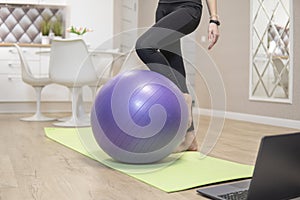 Girls legs stand next to purple fitness ball. quarantine fitness concept