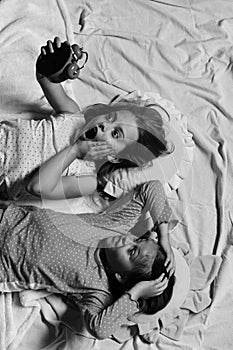 Girls lie on white and pink bed sheets holding clock