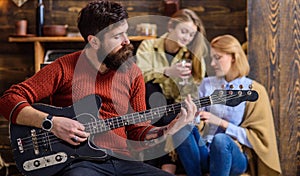 Girls listening to song performed by handsome bearded musician. Guitarist entertaining guests at party. Man with hipster