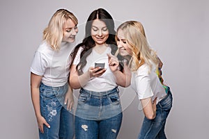 Girls looking at phone screen together.Studio portrait of two girls loking at the mobile phone while blonde girls using