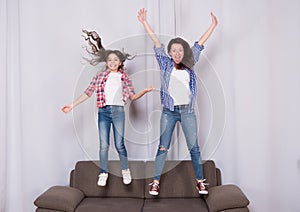 Girls only. Mom and daughter close friends. Mother and cheerful daughter having fun jumping couch. Happy childhood