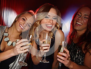 Girls night. Three attractive young friends toasting with glasses of champagne while smiling at the camera.