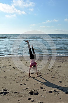 Girls performs handstand on sandy beach on the North Sea coast