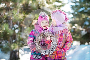 Girls in pink suits hold a Christmas wreath in winter. Children`s winter holidays