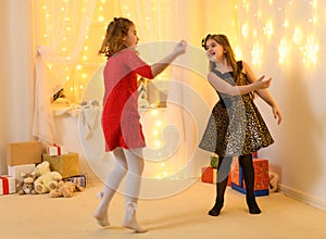 Girls play and dance, home interior decorated with festive lights and gifts