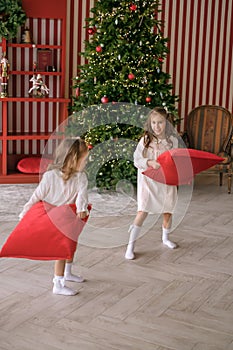 Girls play pillow fight early on xmas morning in room with Christmas tree