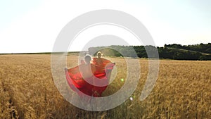 Girls play superheroes running across field with wheat in glare of sunlight. Slow motion