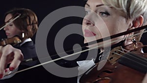 Girls in play the violins in a composition in a room. Black background. Close up