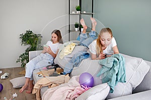 Girls are playing on a mobile phone. The room is a mess. Children scattered things in the room photo