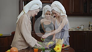 Girls prepare a salad from fresh vegetables for breakfast, standing in a modern kitchen. Young women with towels on