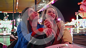 Girls rest amusement park in illuminated carousel closeup. Two smiling friends