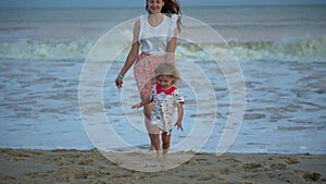 Girls runs to mother on beach. Happy family daughter and mom on sandy seashore. Beautiful sunrise and sunset