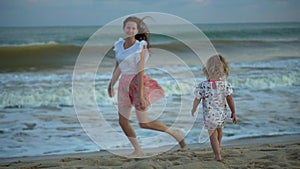 Girls runs to mother on beach. Happy family daughter and mom on sandy seashore. Beautiful sunrise and sunset