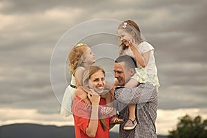 Girls sit on mother father shoulders on cloudy sky