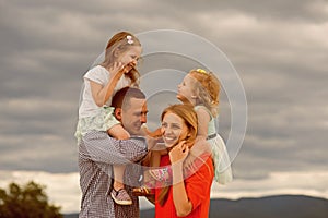 Girls sit on mother father shoulders on cloudy sky