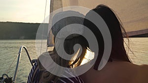 Girls sitting close on sailboat during river trip at sunset