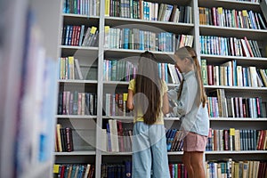 Girls standing near the high book shelves in the school library