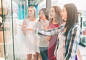 Girls are standing at the showcase of lingerie store and looking at maneken with interest. Brunette is pointing on photo